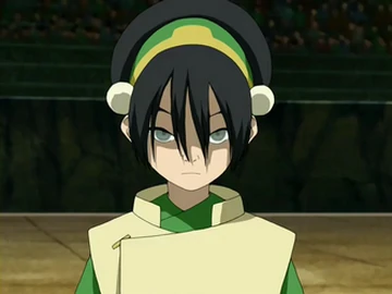 Toph Beifong, a young woman with long dark hair in traditional Earth Kingdom attire, standing confidently with a determined expression. She wears green and gold clothing reflecting her status as an earthbender master. The background shows a neutral setting that emphasizes her strong and assured presence.